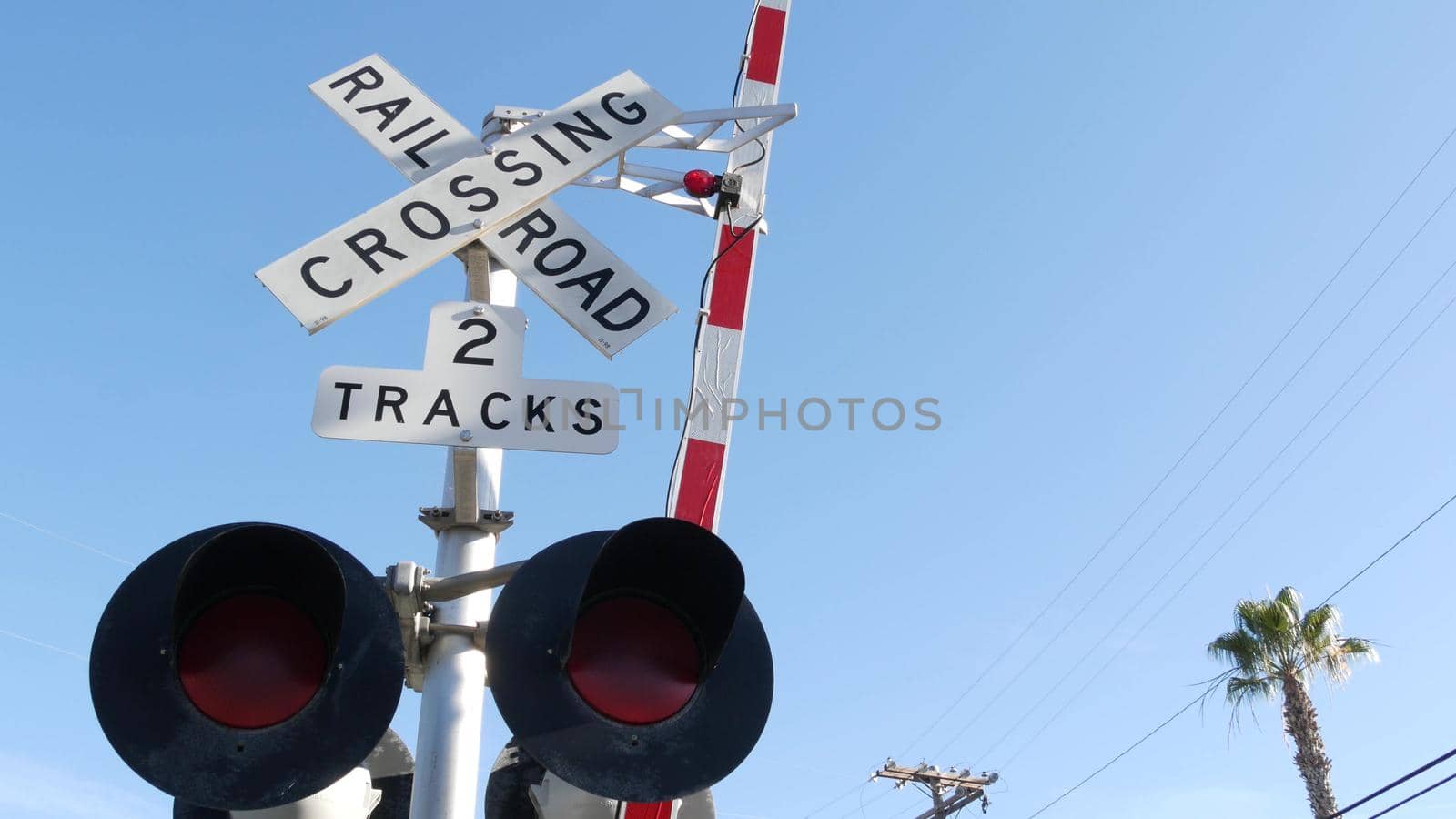 Level crossing warning signal in USA. Crossbuck notice and red traffic light on rail road intersection in California. Railway transportation safety symbol. Caution sign about hazard and train track.