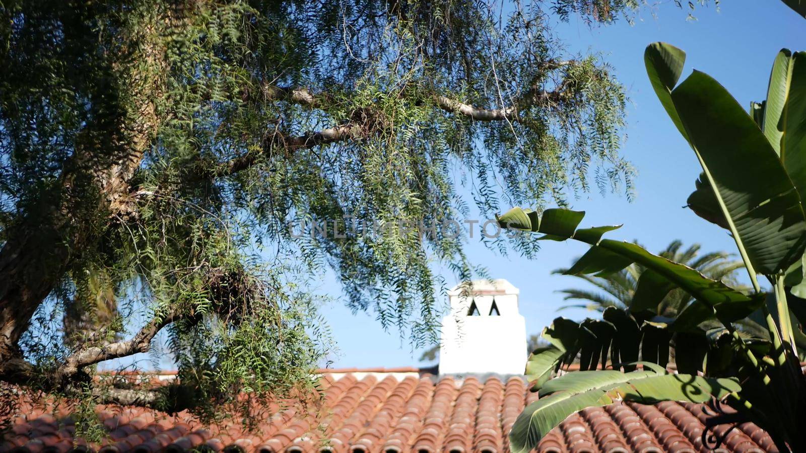 Mexican colonial style suburban, hispanic house exterior, green lush garden, San Diego, California USA. Mediterranean terracotta ceramic clay tile on roof. Rustic spanish tiled rooftop. Rural details.