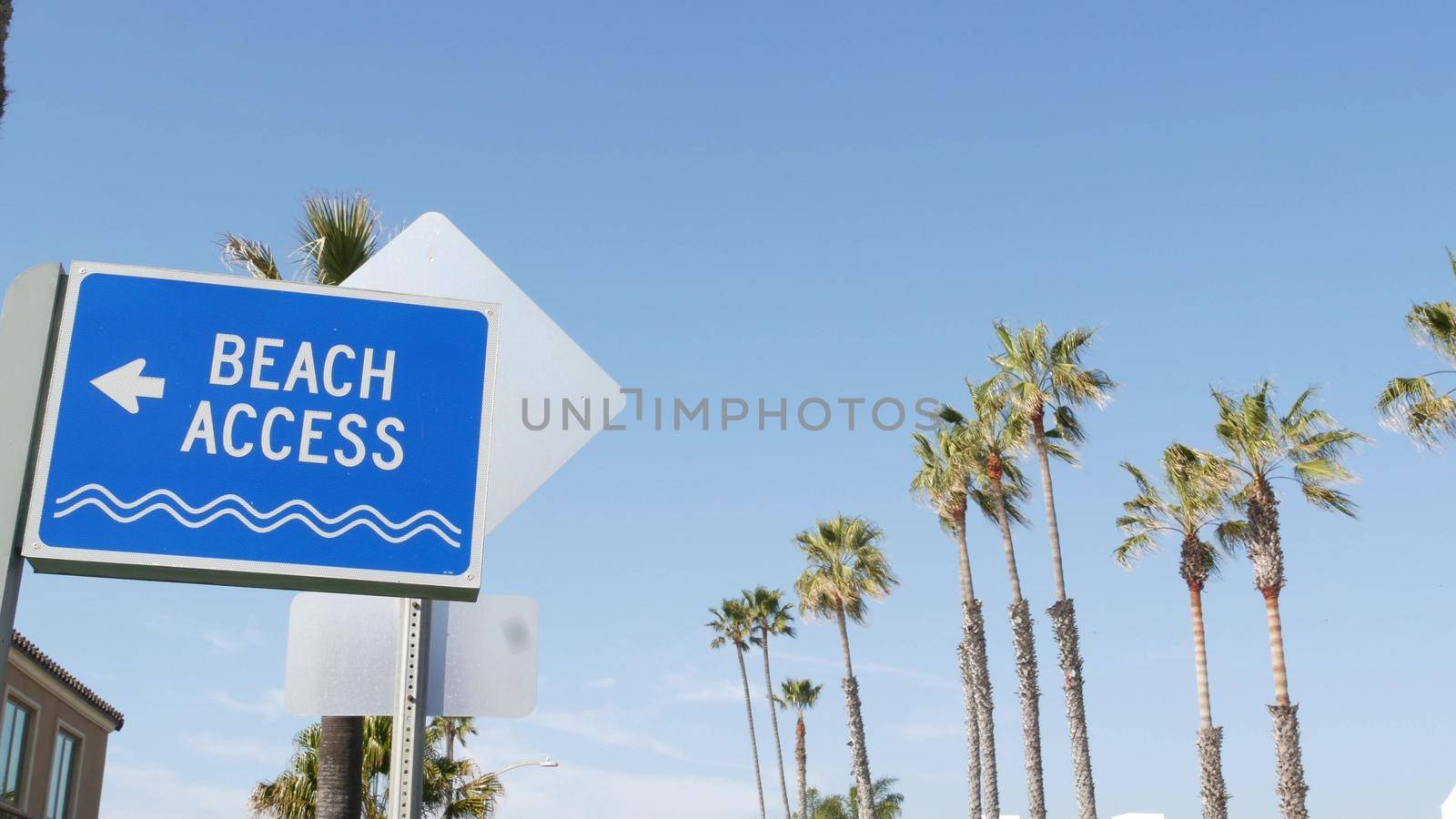 Beach sign and palms in sunny California, USA. Palm trees and seaside signpost. Oceanside pacific tourist resort aesthetic. Symbol of travel holidays and summertime vacations. Beachfront promenade.