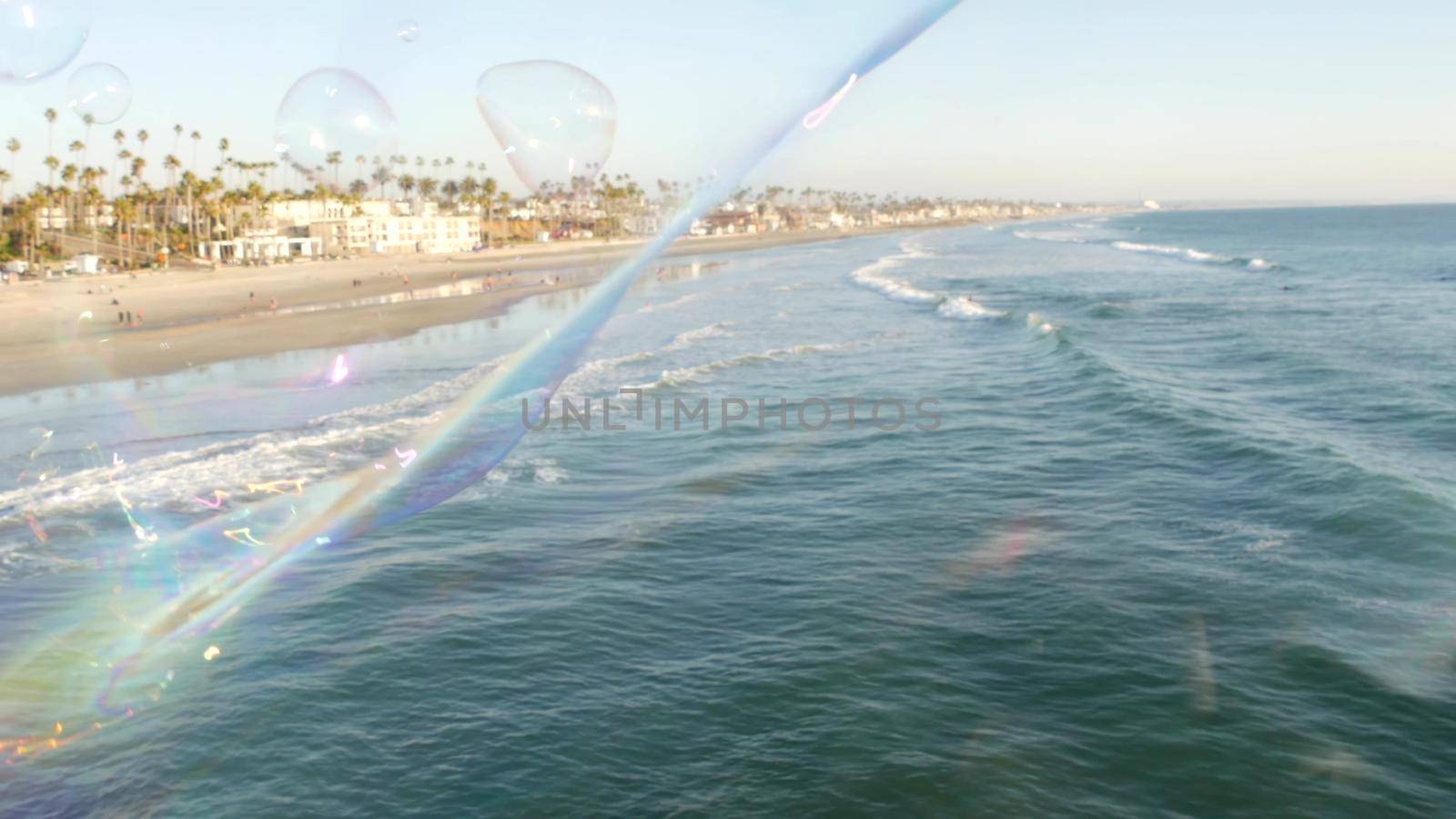 Blowing soap bubbles on ocean pier in California, blurred summertime background. Creative romantic metaphor, concept of dreaming happiness and magic. Abstract symbol of childhood, fantasy, freedom.