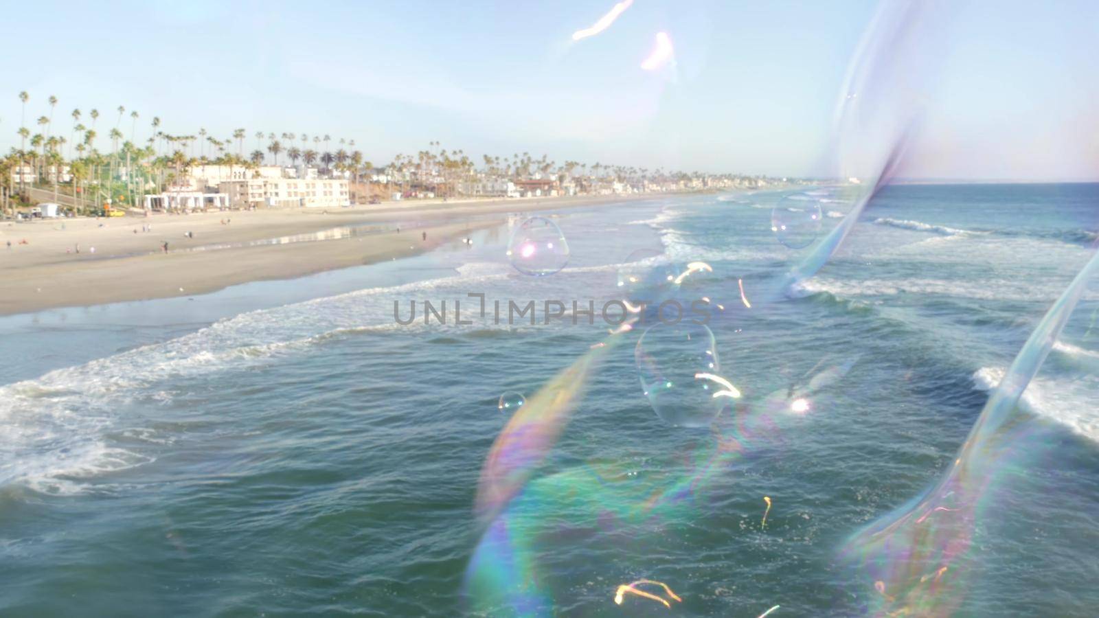 Blowing soap bubbles on ocean pier in California, blurred summertime background. Creative romantic metaphor, concept of dreaming happiness and magic. Abstract symbol of childhood, fantasy, freedom.