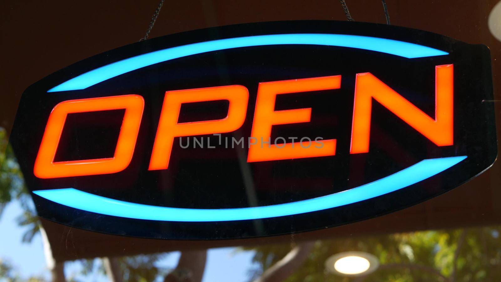 Open neon sign glowing in the dark. Vivid retro styled text at entrance on glass window. Colorful electric banner selective focus close up. Light bulbs radiance at night. Shiny illuminated lettering.