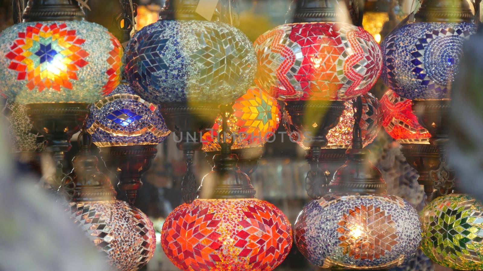 Colourful turkish lamps from glass mosaic glowing. Arabic multi colored authentic retro style lights. Many illuminated moroccan craft lanterns. Oriental islamic middle eastern decor. Shiny folk shop by DogoraSun