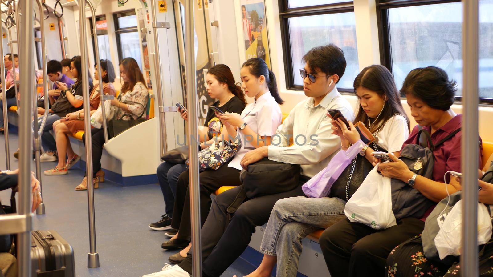 BANGKOK, THAILAND - 13 JULY, 2019: Asian passengers in train using smartphones. Thai people online surfing internet in bts car. Public transportation. Addiction from social media and phone in subway. by DogoraSun