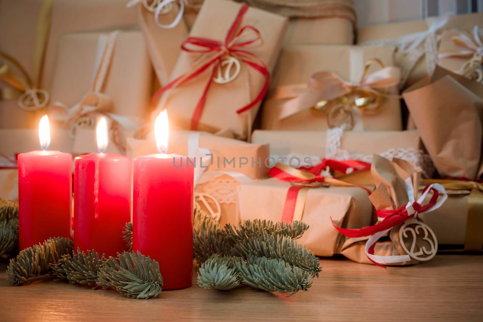 Heap of decorated advent gift boxes in craft paper with red and white decor in a heap on the room floor three red burning candles and fir tree branch