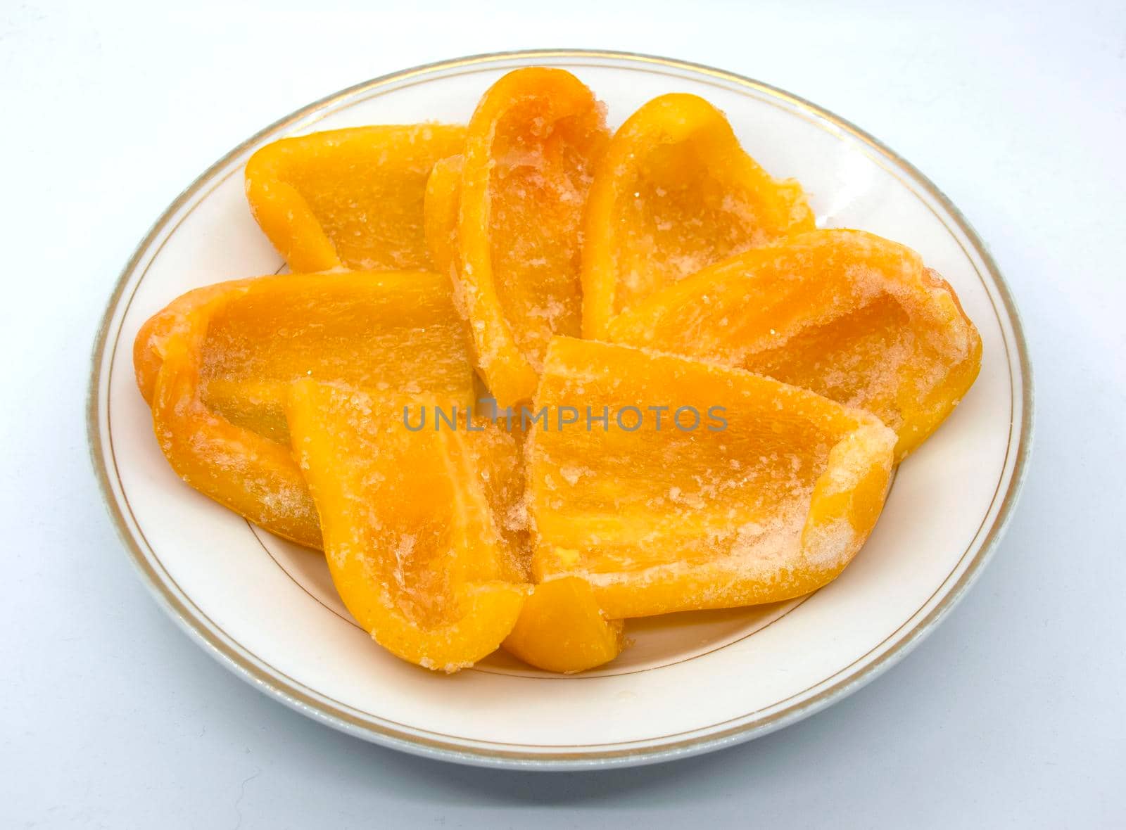 On a white plate lies frozen yellow bell pepper sliced into wedges.