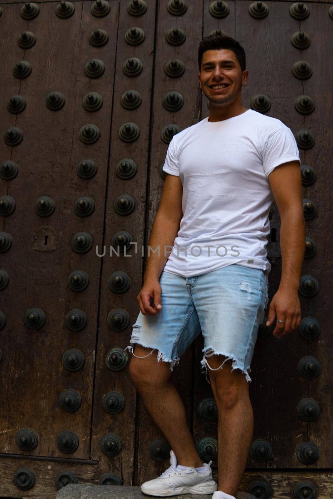 Man with a white T-shirt and a brown door in the background by xavier_photo