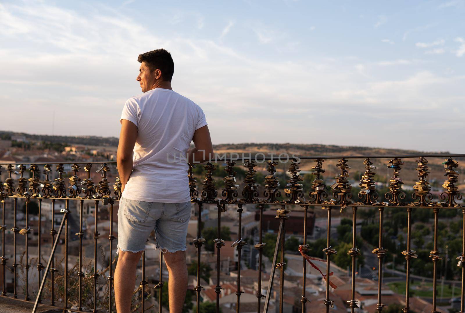 Boy with white T-shirt and brown hair on his back facing a village