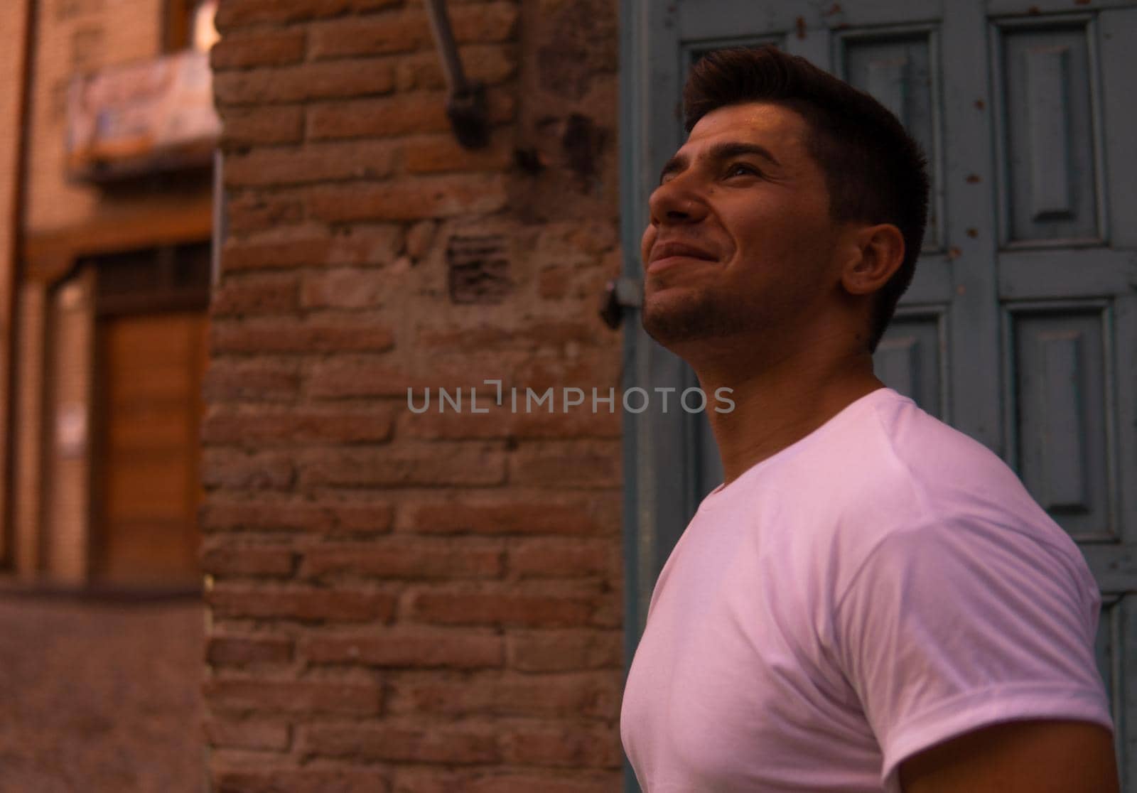 Man with a white T-shirt and a brown door in the background modeling and intense look