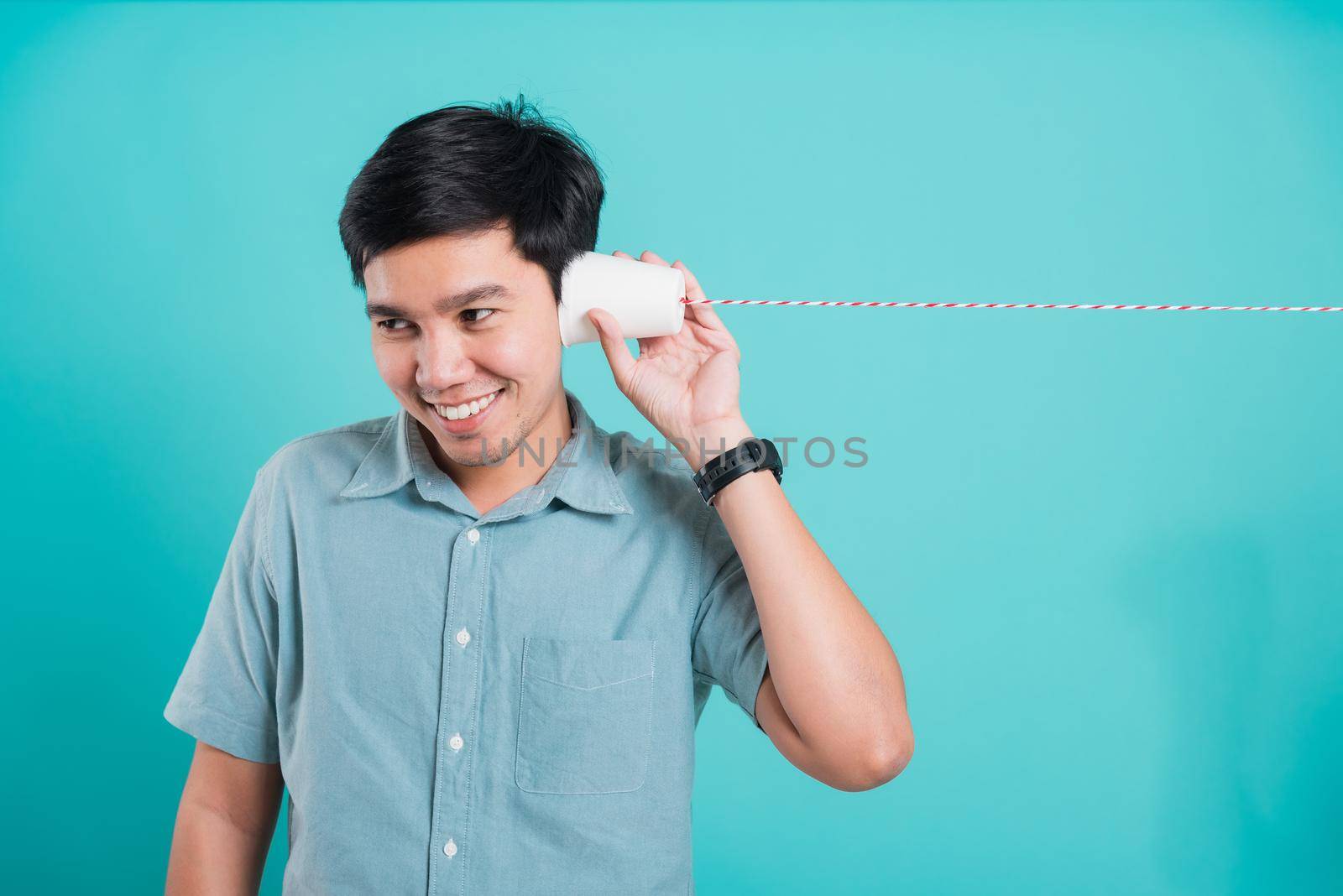 Portrait happy Asian handsome young man smile white teeth standing wear shirt, He holding paper can telephone for listening the message, studio shot on blue background