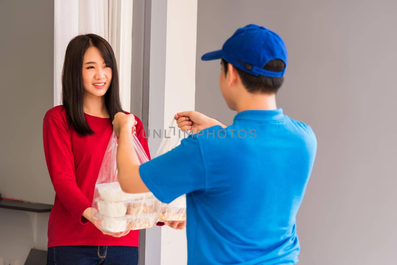 Asian young delivery man in blue uniform he making grocery service giving rice food boxes plastic bags to woman customer receiving front house under pandemic coronavirus, Back to new normal concept