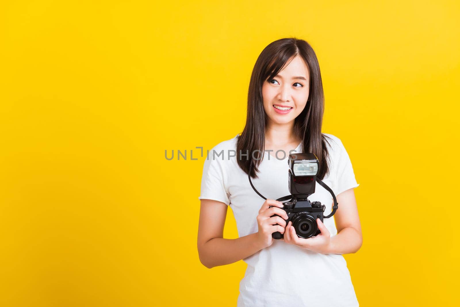 Portrait of happy Asian beautiful young woman photographer holding vintage digital mirrorless photo camera on hands, studio shot isolated on yellow background, lifestyle teenager hobby travel concept