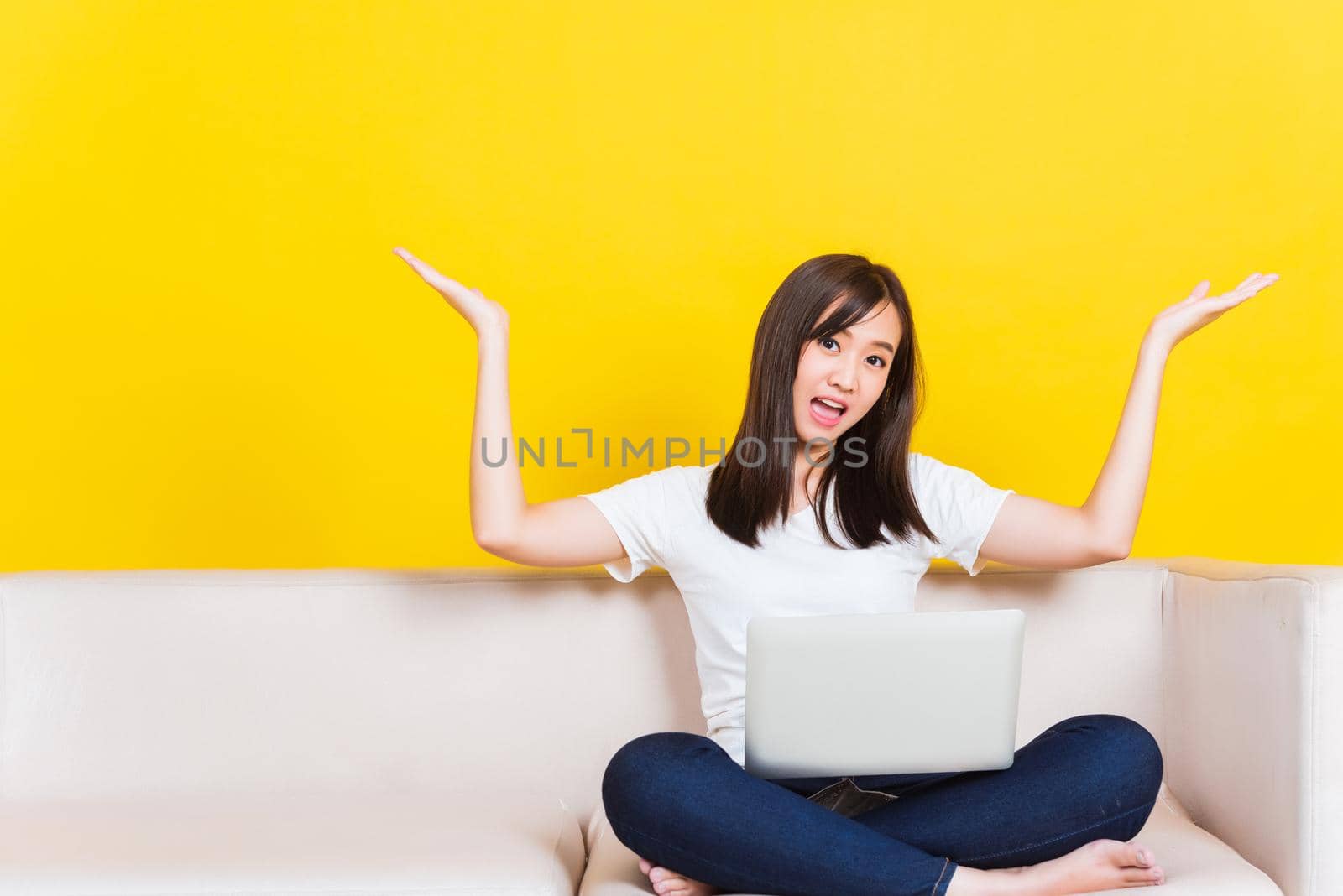 Portrait Asian of happy beautiful young woman work from home she sitting on sofa using laptop computer in house living room raise hand up away studio shot isolated on yellow background