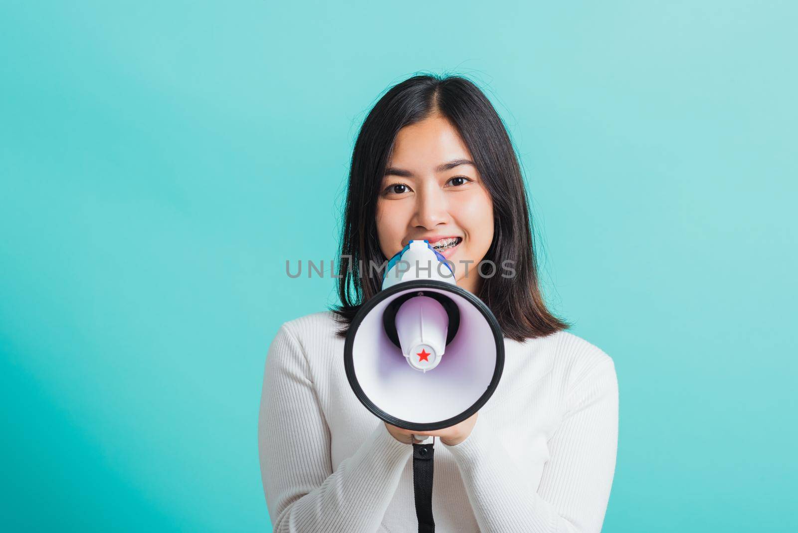 Beautiful Asian woman smile she holding megaphone making the announcement, female excited cheerful announce good news isolated on a blue background