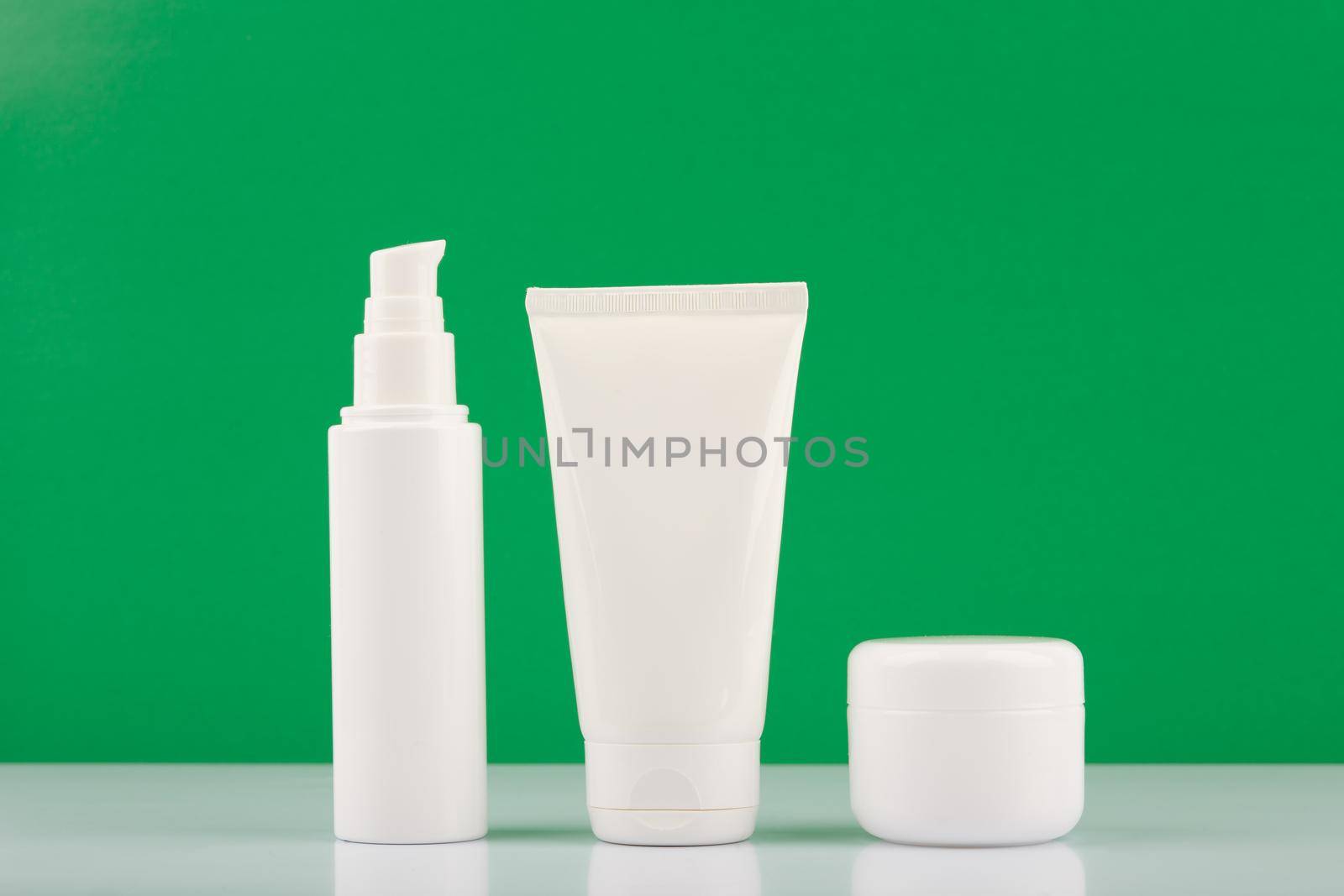 Organic cosmetic products set for daily beauty routine on white glossy table against green background by Senorina_Irina