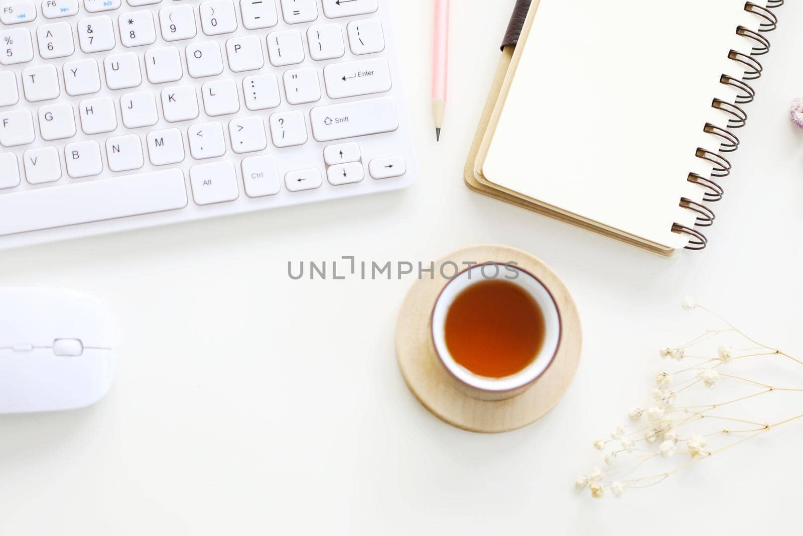 Red tea and spiral notebook with pencil and mouse and keyboard with dry flower