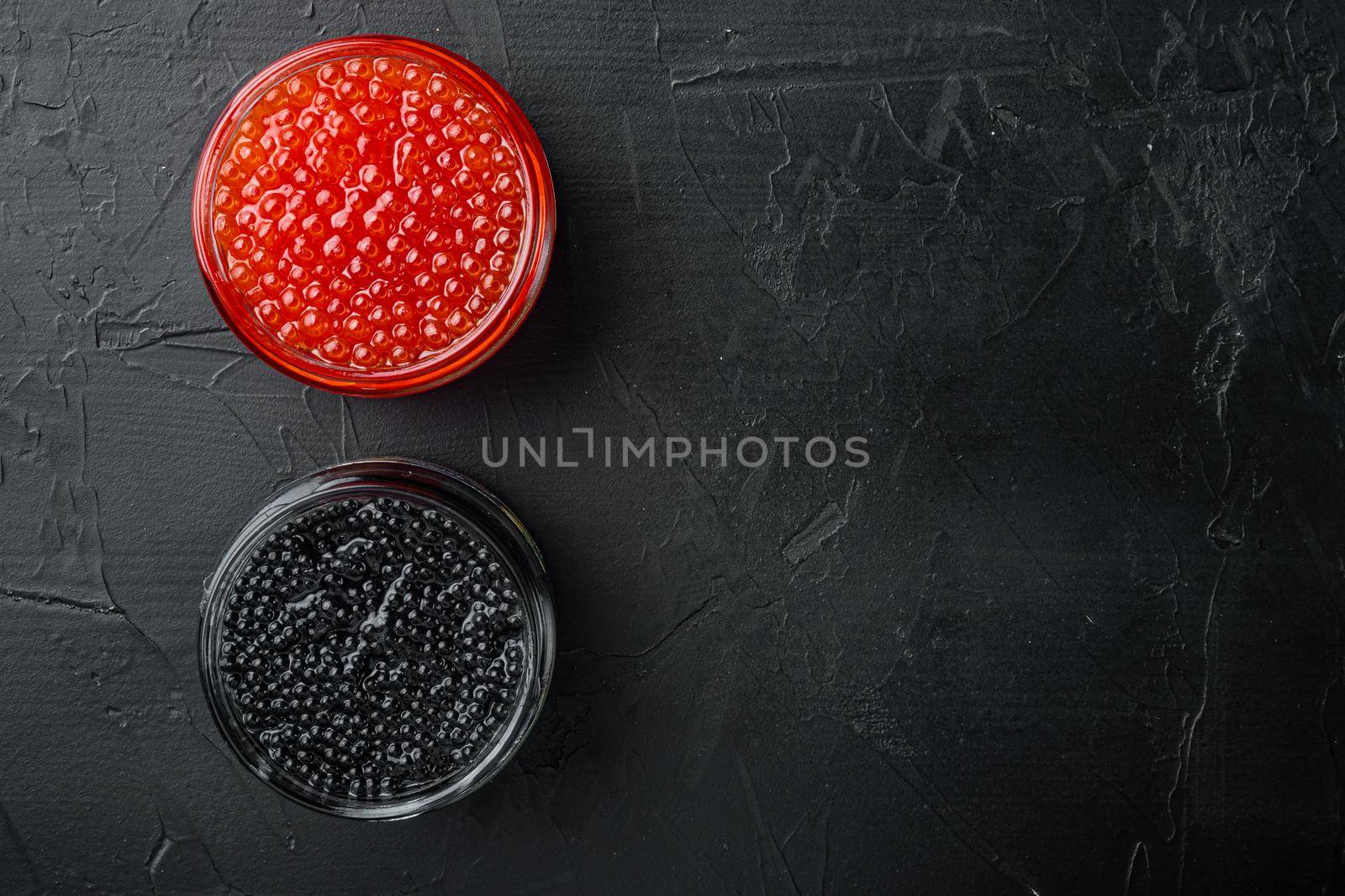 Red and black caviar in glass bowl, on black background, top view flat lay with copy space for text