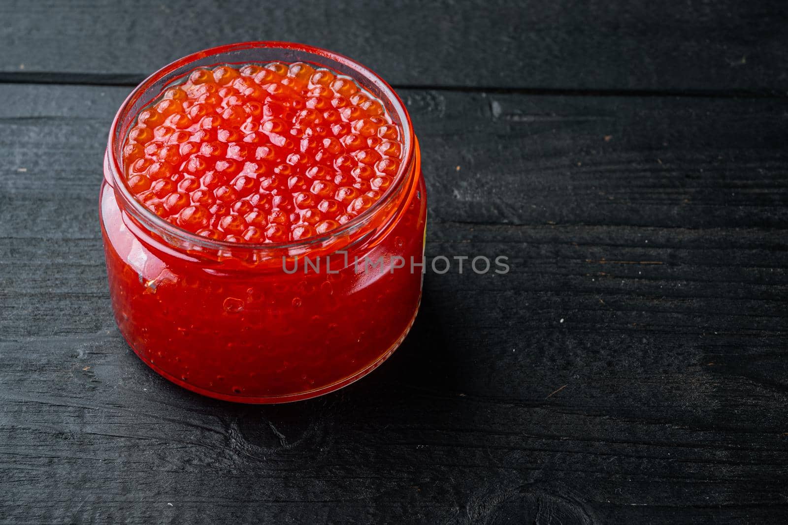 Glass with delicious red caviar, on black wooden table background with copy space for text