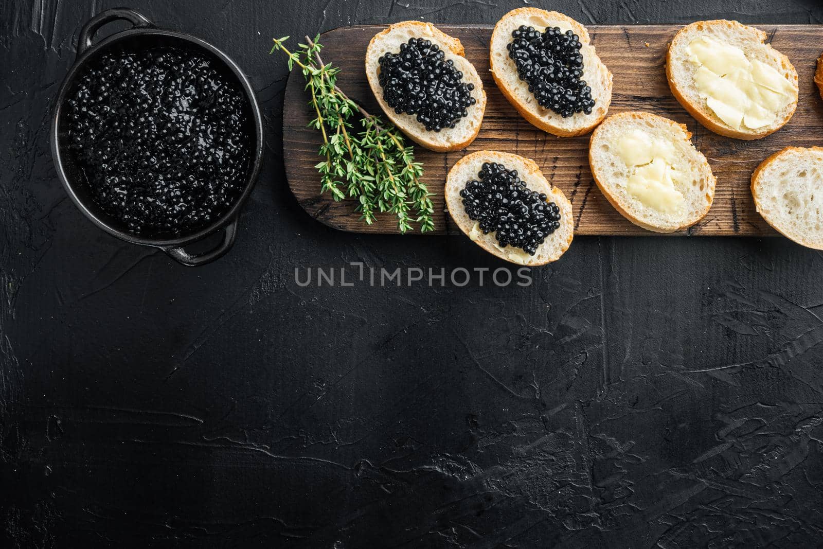 Black caviar served on baguettes, on black background, top view flat lay with copy space for text