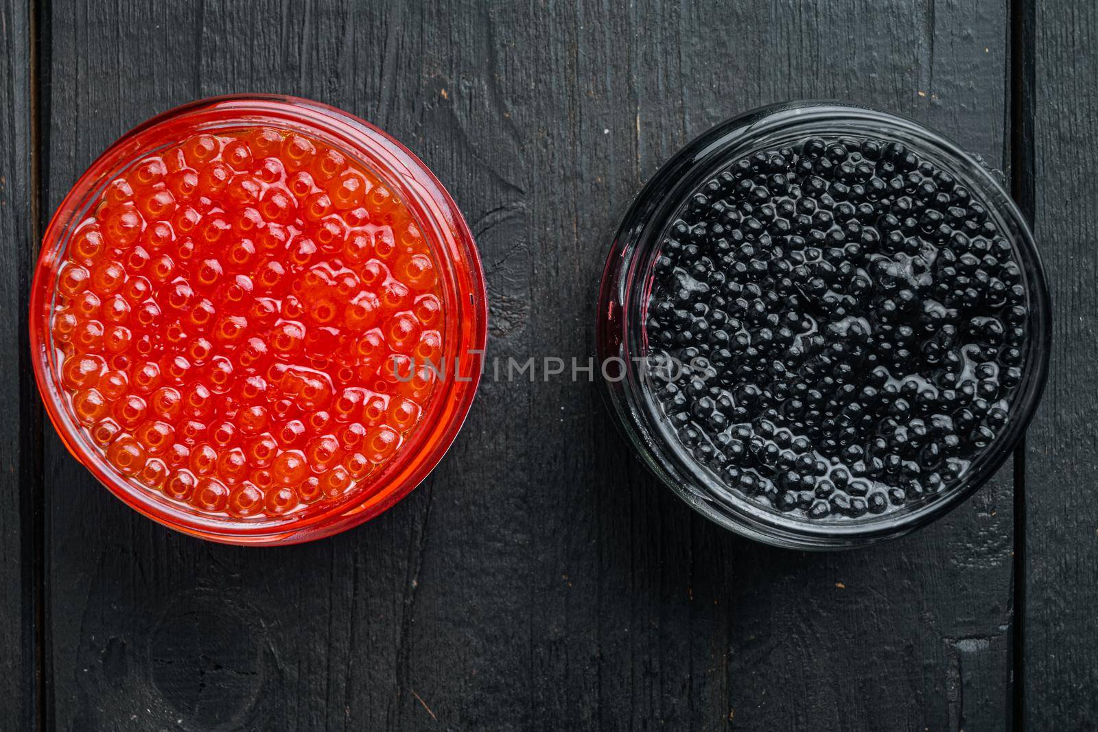 Glass jar with black and red caviar, on black wooden table background, top view flat lay