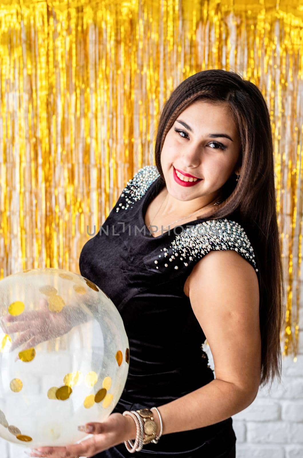 Beautiful brunette woman in black party dress celebrating her birthday holding balloon by Desperada