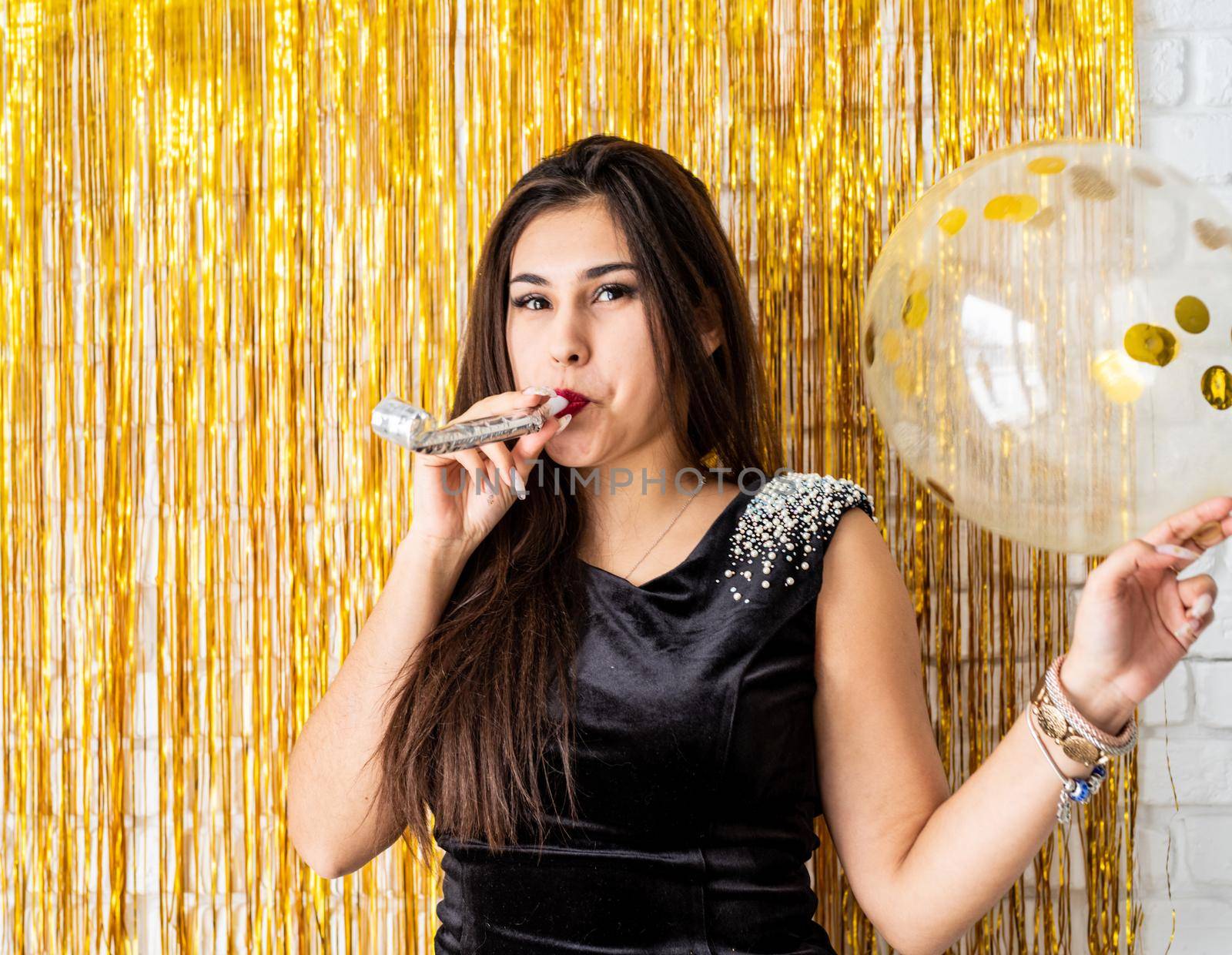 Birthday party. Beautiful brunette woman in black party dress celebrating her birthday blowing the noise maker