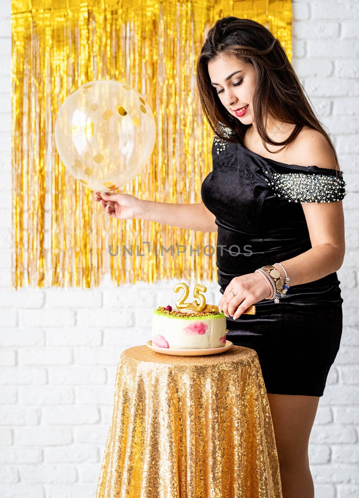 Birthday party. Beautiful brunette woman in black party dress holding ballooncelebrating her birthday cutting the cake