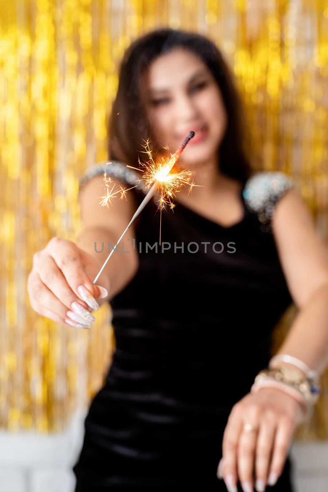 Birthday party. Beautiful young woman holding sparkler and balloon on golden background