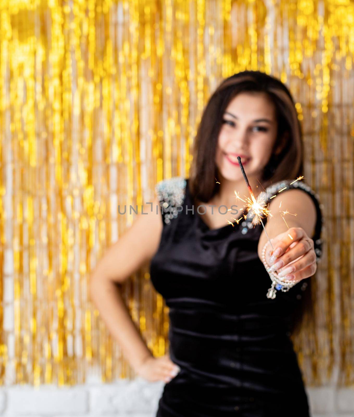Beautiful young woman holding sparkler and balloon on golden background by Desperada