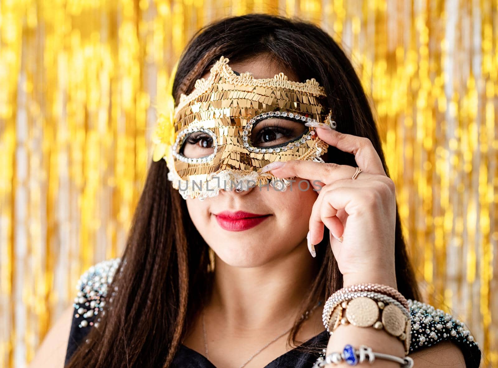 Birthday party. Beautiful brunette woman in black party dress wearing shiny golden masquerade mask