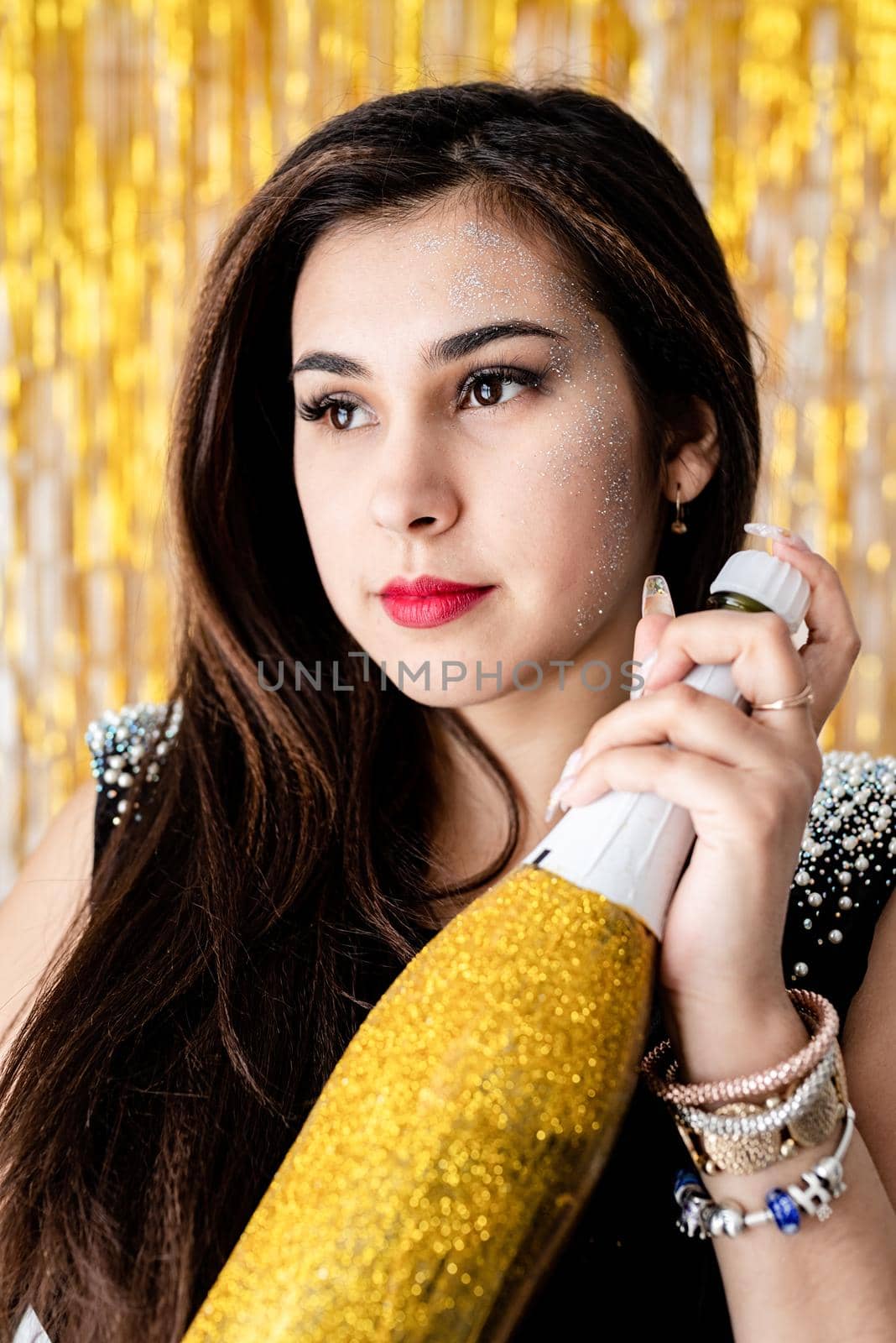 Beautiful brunette woman in black party dress celebrating her birthday holding balloon and champagne bottle by Desperada