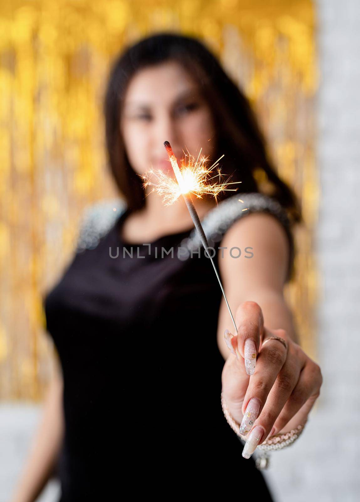 Birthday party. Beautiful young woman holding sparkler and balloon on golden background