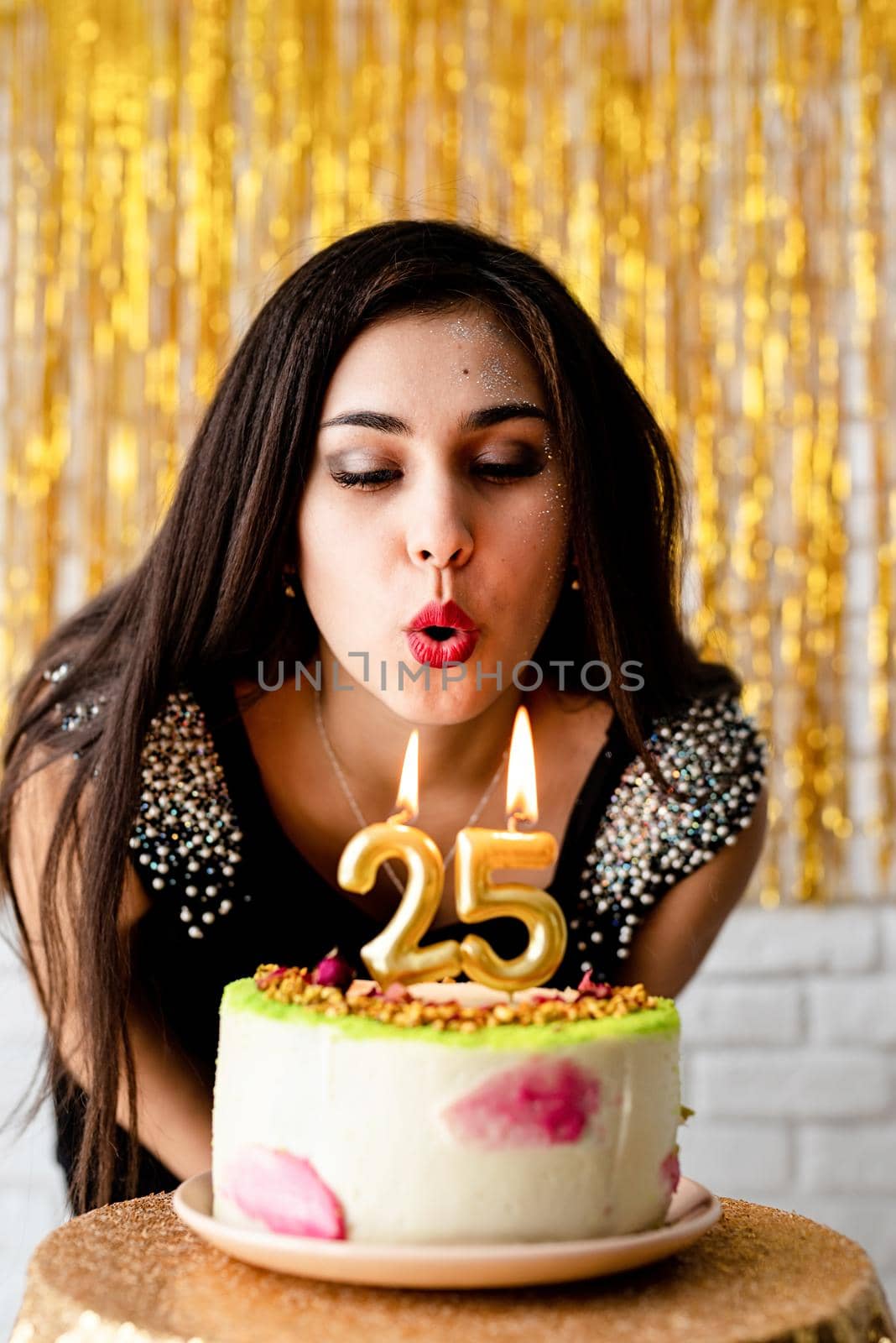 Attractive caucasian woman in black party dress blowing candles on birthday cake by Desperada