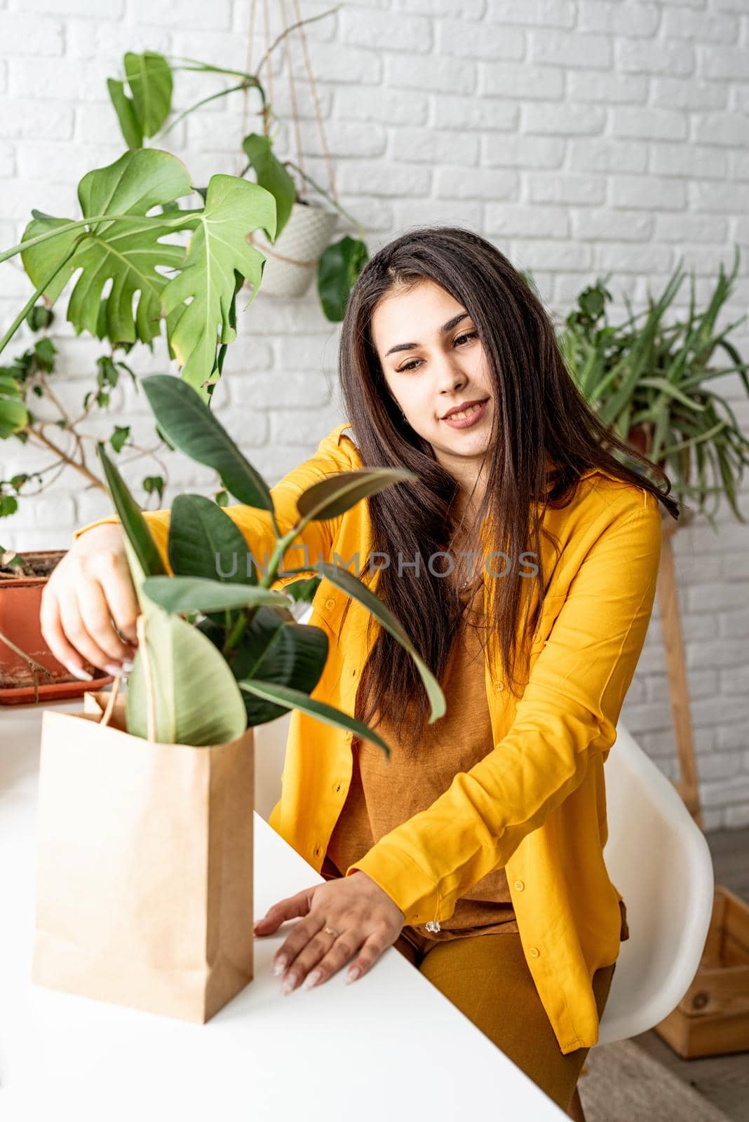 Home gardening. Small business. Young woman gardener taking care of the plants putting a flowerpot to the craft bag ready to sell it