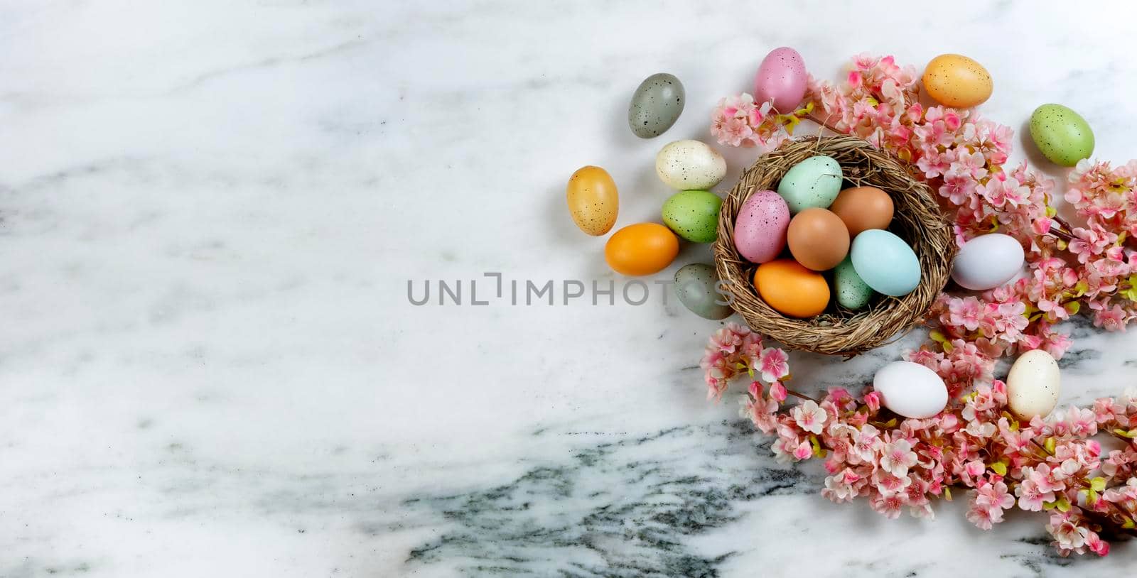 Happy Easter holiday concept with nest of colorful eggs with pink cherry blossom flowers on stone background in overhead view 