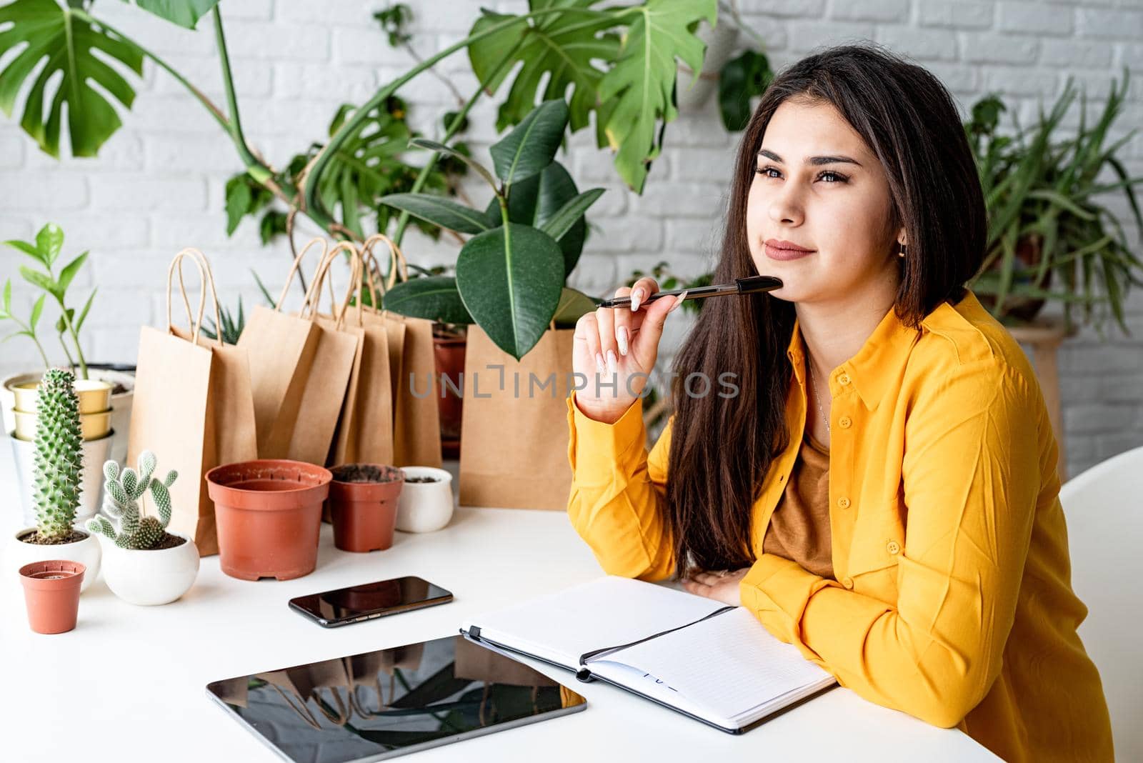 Young smiling woman gardener making notes in the notepad surrounded with plants by Desperada