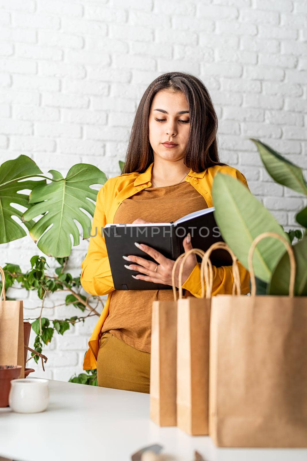 Young woman gardener making notes in the notepad surrounded with plants by Desperada