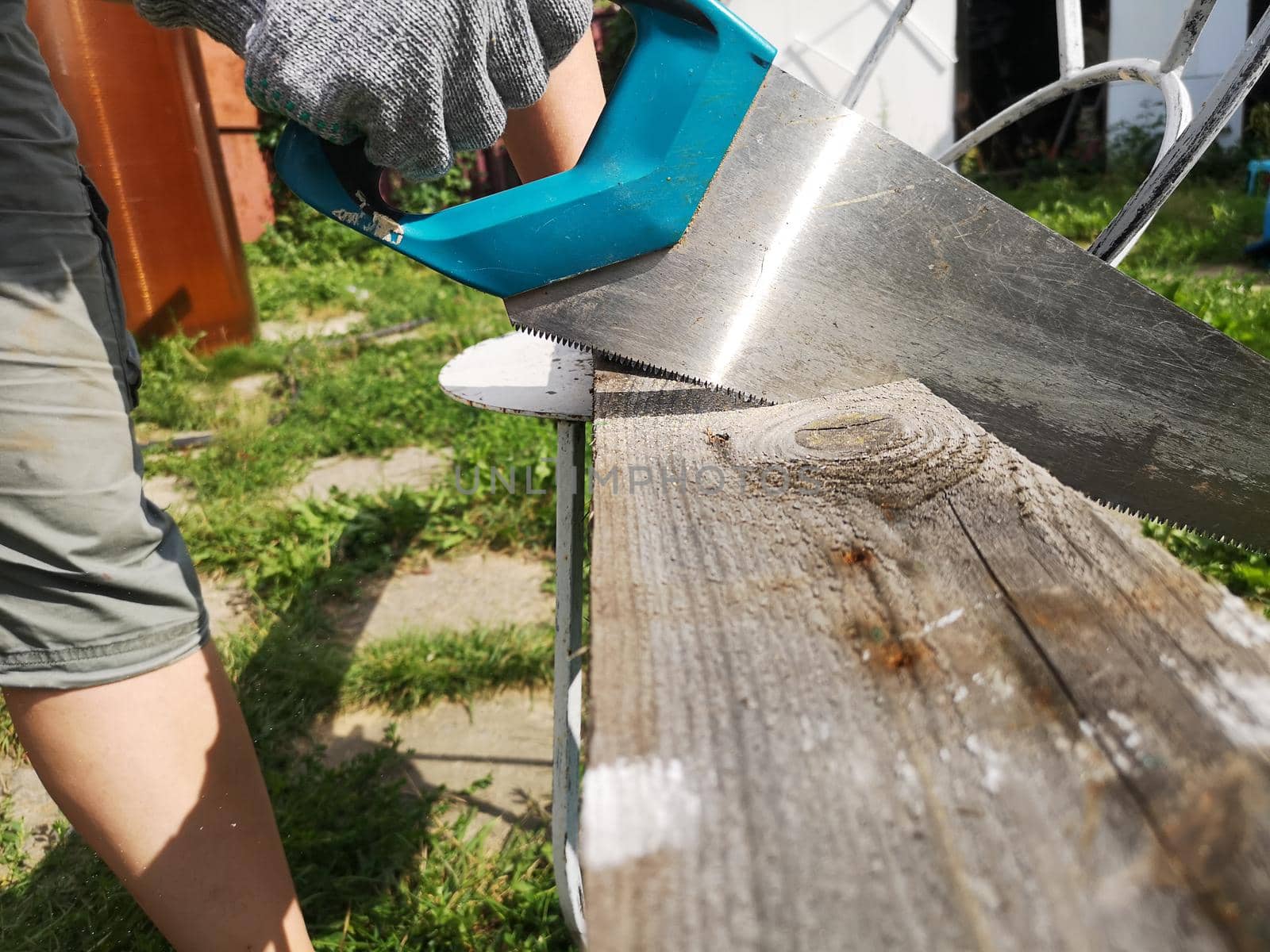 Farmer hand with saw cutting wooden boards in the garden.