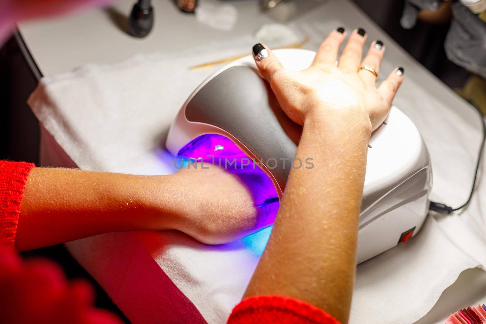 Woman's hand in a lamp for manicure. Dries nails after polishing. by Yurich32