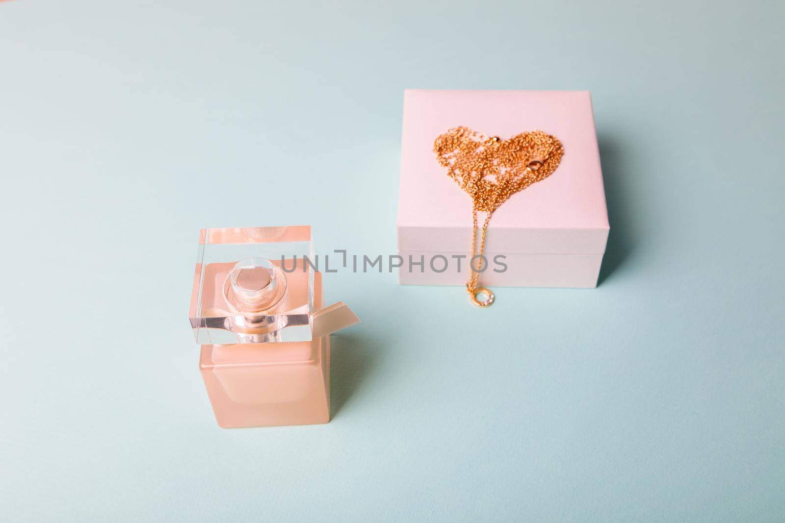 A gift for Valentine's Day. Perfume and a box with a gold chain on a blue background. Chain in the shape of a heart.