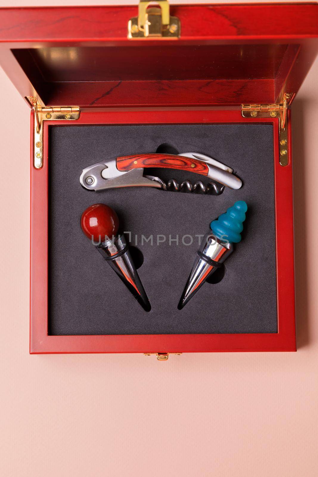 Gift set of corkscrew and removable lids. Wine corks and bottle openers in a wooden box on a pink background.