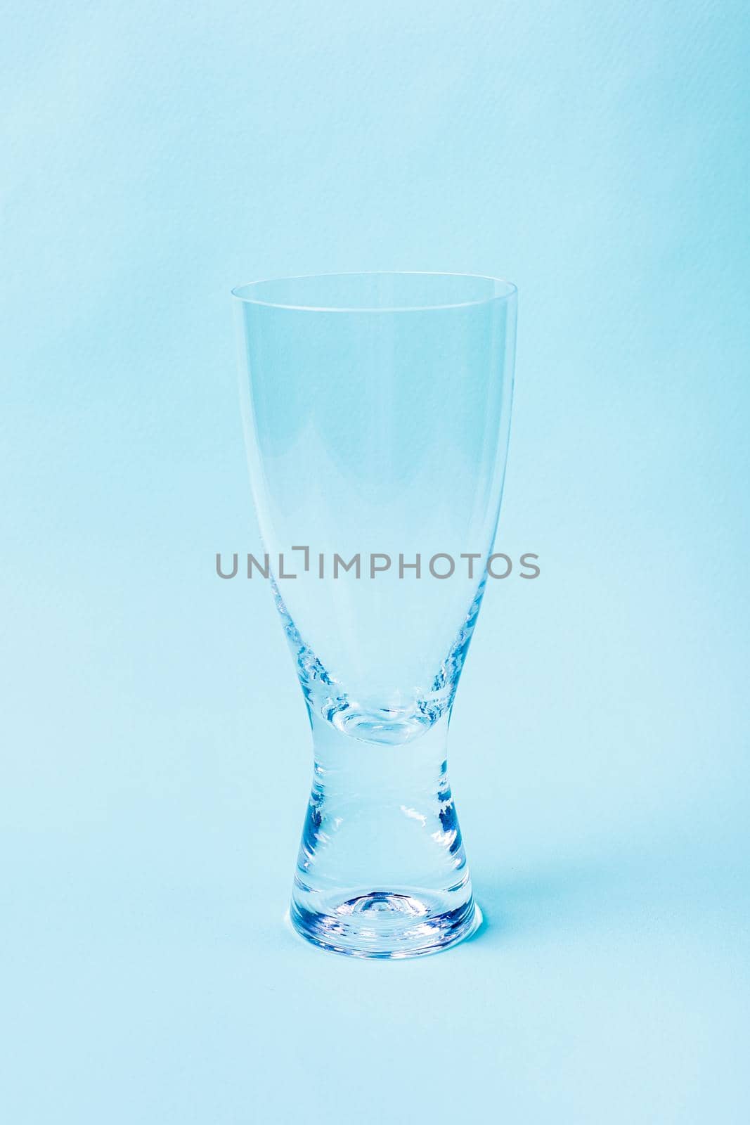 Empty glass from transparent glass on a blue background. For drinking, thirst quenching, kitchen utensils, dishes.