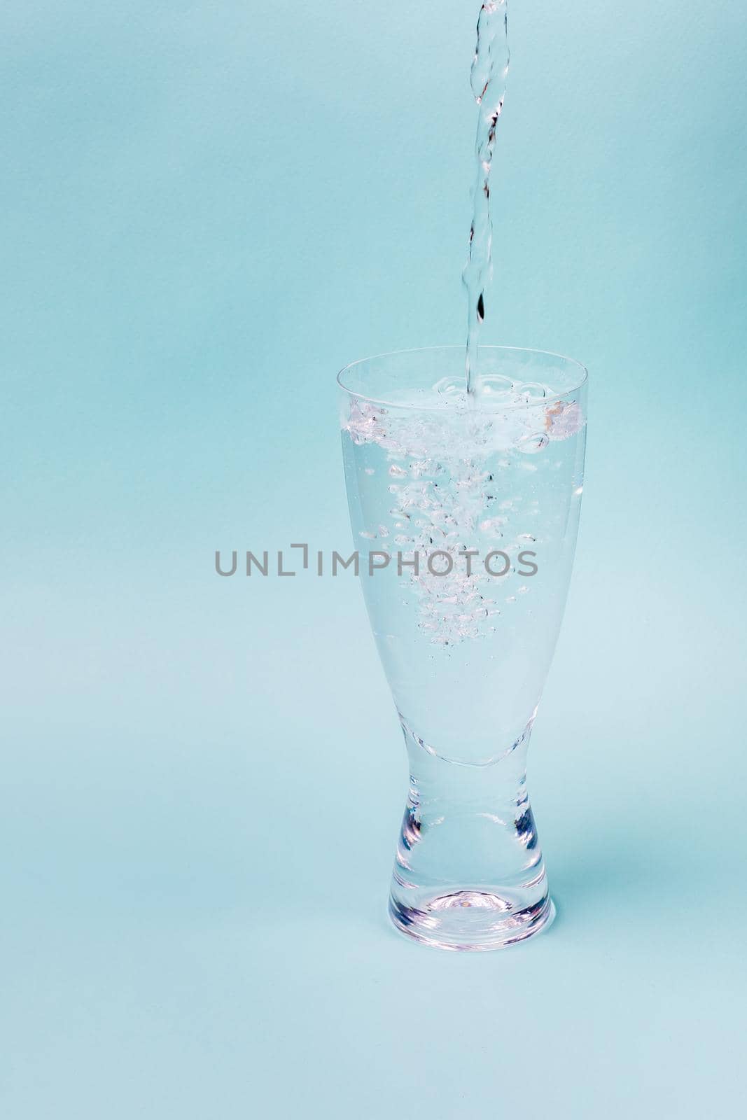 A jet of water fills transparent glass against a blue background. White bubbles rise.