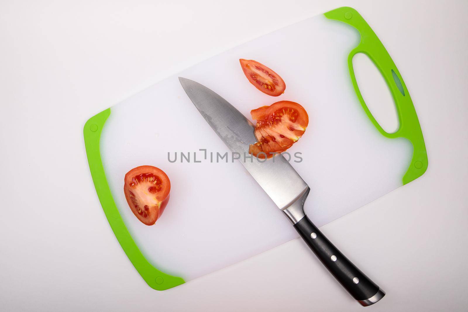 On a cutting board is a fresh red cut tomato and a large chef's knife. On an isolated white background.