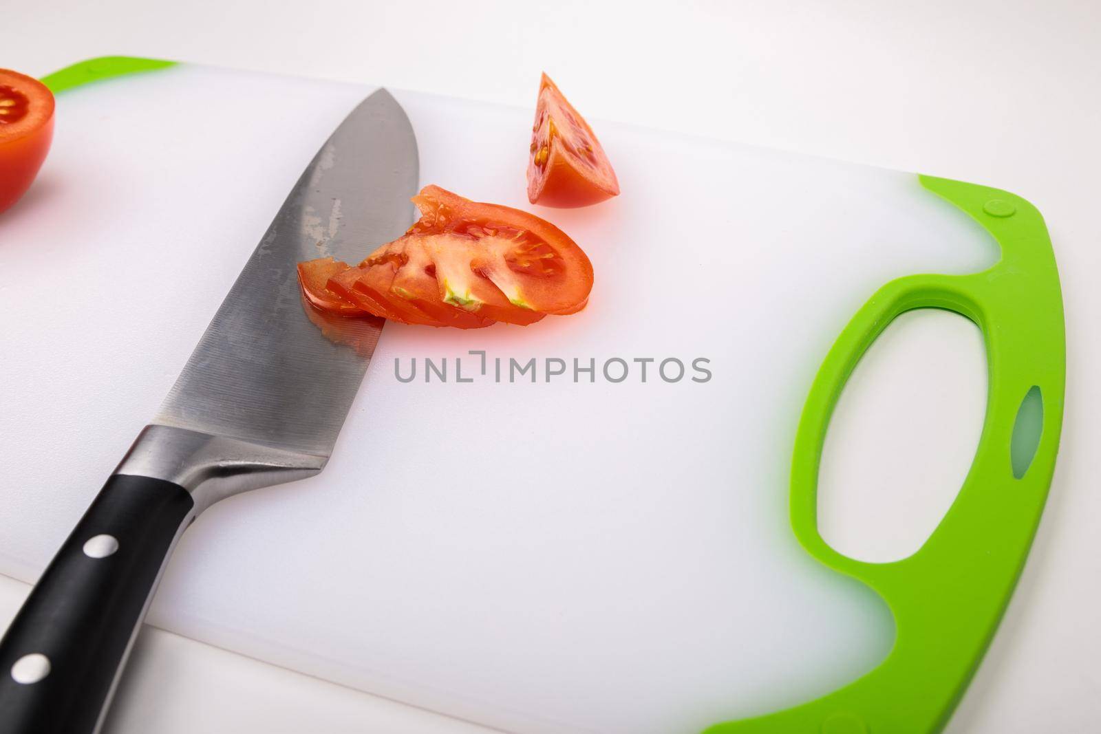 On a cutting board is a fresh red cut tomato and a large chef's knife. On an isolated white background.