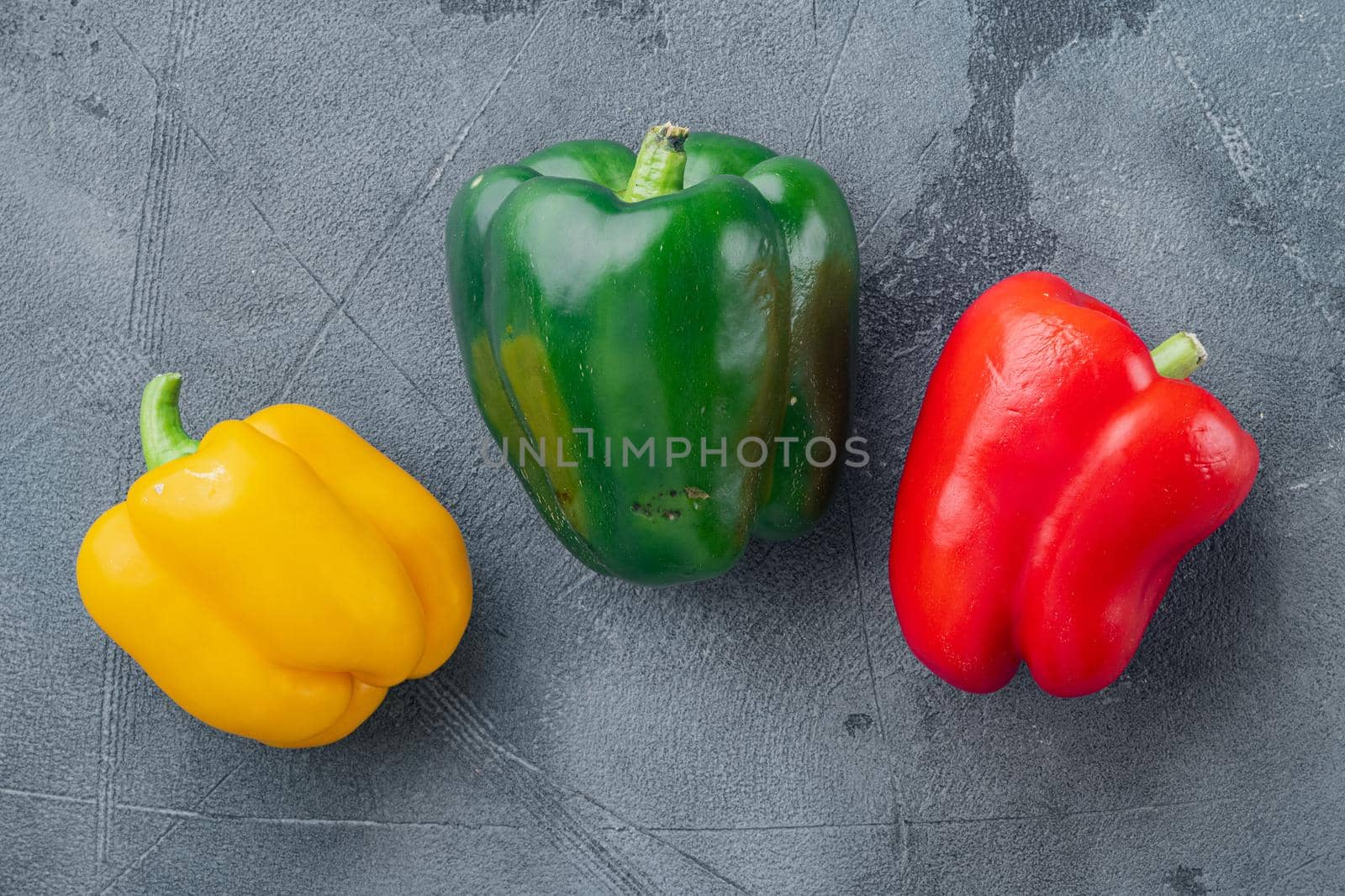 Green , yellow and red bell peppers, on gray background, top view flat lay