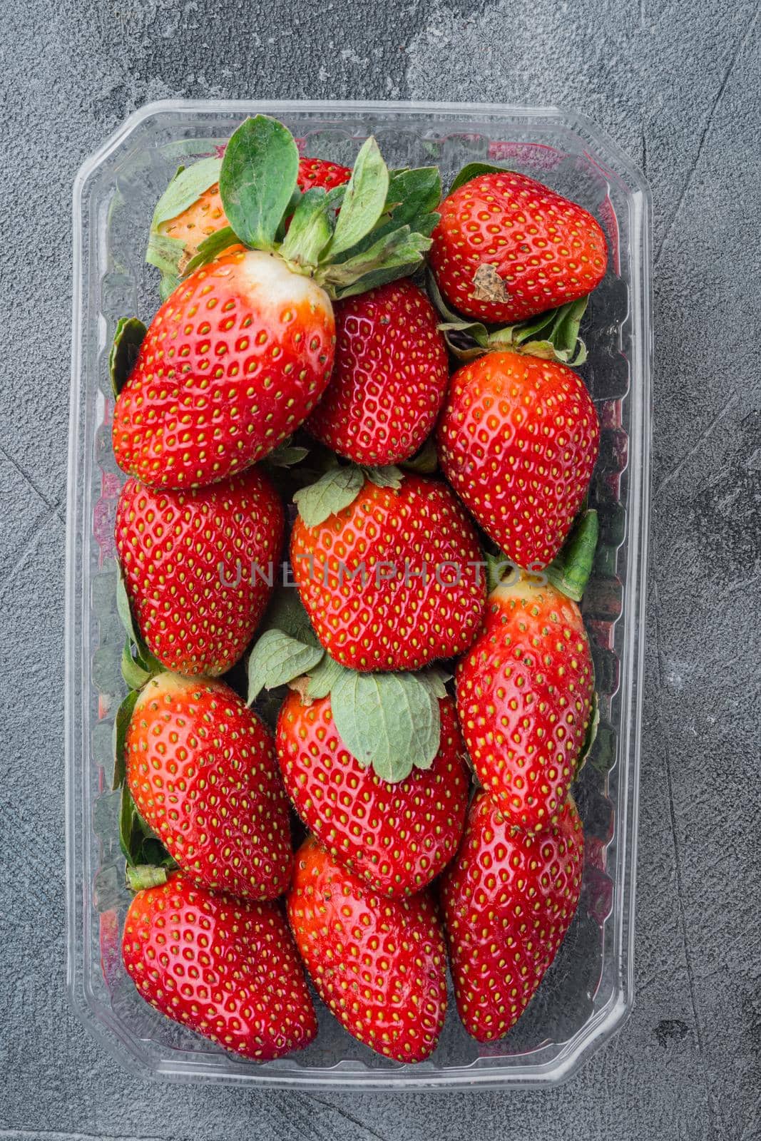 Transparent plastic tray, with freshly picked strawberries, on gray background, top view flat lay