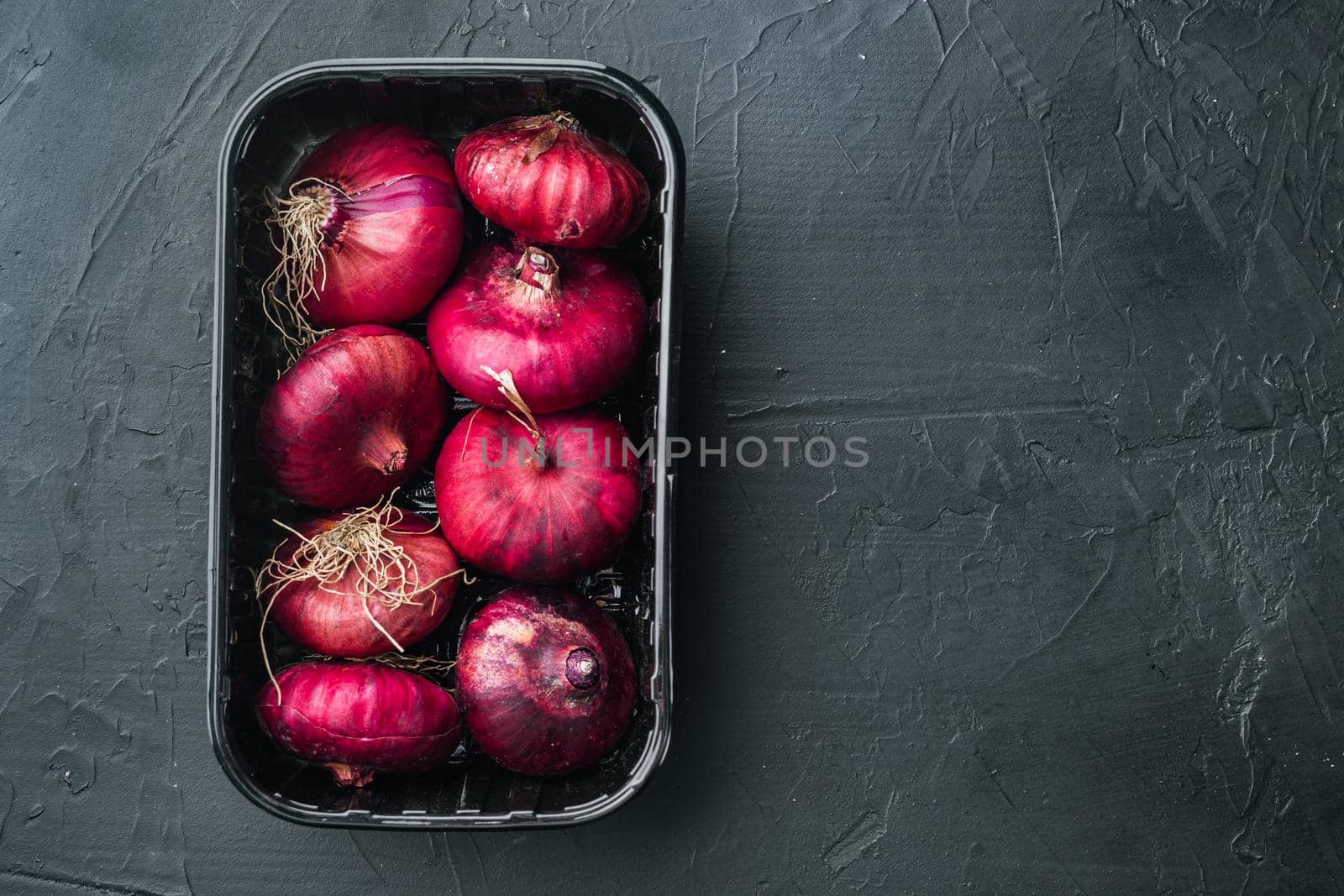 Fresh whole red onions, on black background, top view flat lay with copy space for text