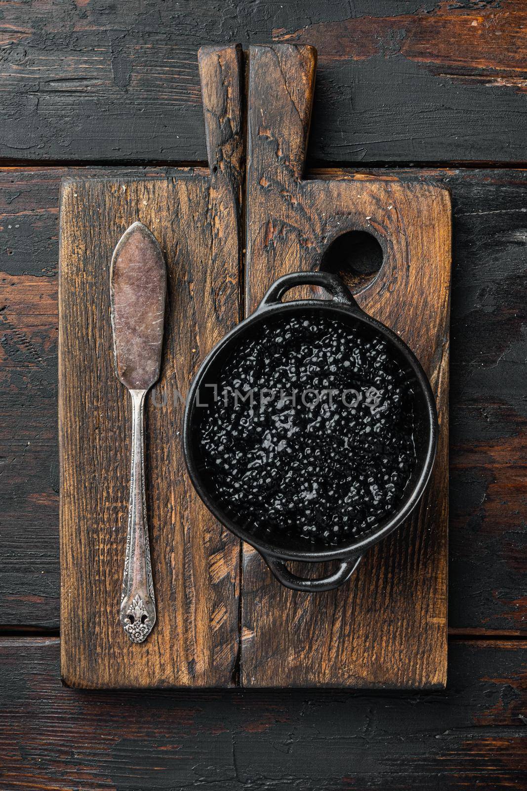 Black bowl of black caviar, on old dark wooden table background, top view flat lay
