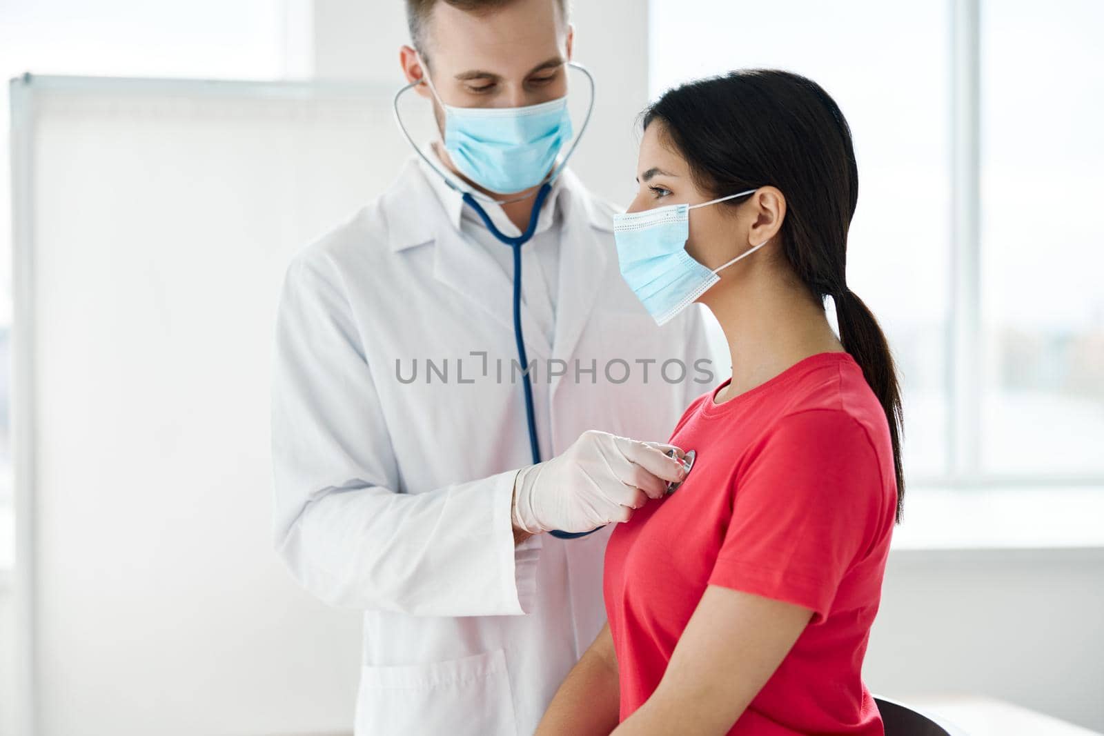 doctor in a medical mask stands next to a woman in a red t-shirt chest examination breathing. High quality photo